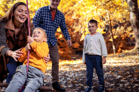 Happy family having fun on a swing in the autumn parkの写真素材