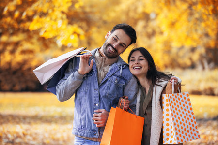 Couple comes back from shopping at the mall. Walking through the colorful park with shopping bags.の写真素材