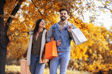 Couple comes back from shopping at the mall. Walking through the colorful park with shopping bags.の写真素材