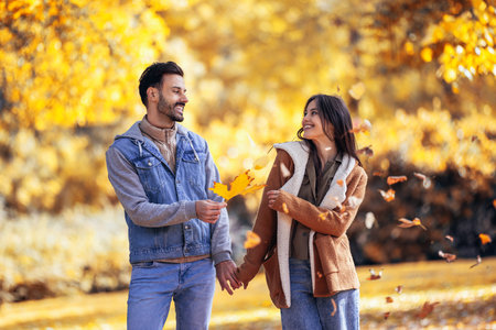 Happy couple walks through the colorful park. They are holding orange leaves on an autumn day.の写真素材