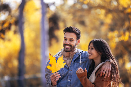 Happy couple walks through the colorful park. They are holding orange leaves on an autumn day.の写真素材