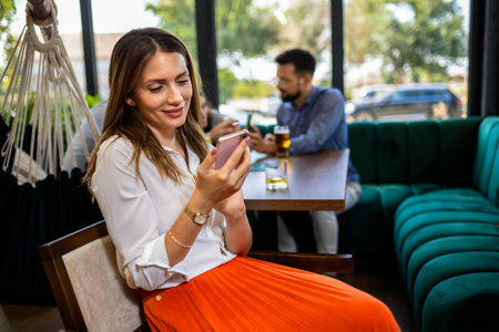 Woman using her phone in the restaurant. Her friends are in the background.の写真素材