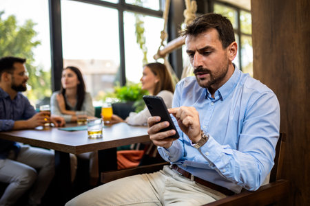 Stressed businessman using his phone in the restaurant with his friends in the backround.の写真素材