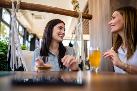 Two girl best friends having out at the restaurant. Drinking coffee and orange juice. They gossip, laugh and have fun time.の写真素材