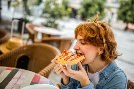 Young ginger girl biting slice of delicious looking pizza.の写真素材