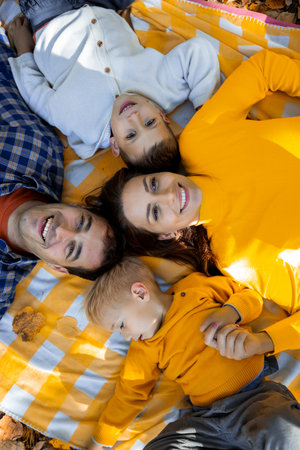 Happy family with two young sons lying on a blanket during an autumn picnic in the park. They are all looking at the camera, smilingの写真素材