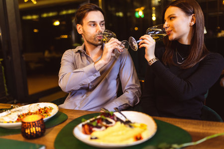 Young, happy couple in love drinks white wine in luxury restaurant on a romantic date .