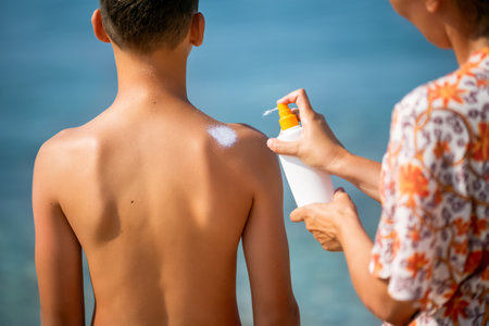 Mother putting sunscreen on the back of her son. Sunny warm day on the beach.の写真素材