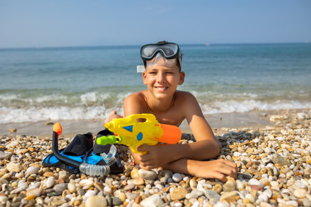 Boy portrait at the beach. He has water gun and equipment for diving in the sea.の写真素材