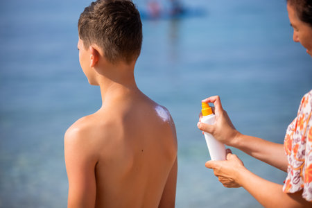 Mother putting sunscreen on the back of her son. Sunny warm day on the beach.の写真素材