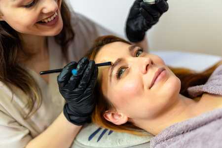 Beauty professional applying eyebrow tint to a woman's brows using a fine brush.の写真素材