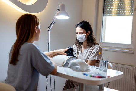 Professional  manicurer using electric machine in beauty salon. Woman in the beauty salon getting her nails done.の写真素材