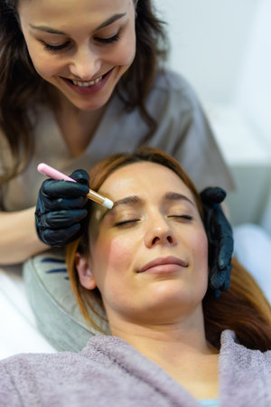 Beauty professional applying eyebrow tint to a woman's brows using a fine brush.の写真素材