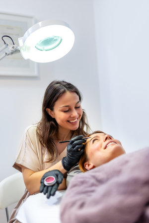 Beauty professional applying eyebrow tint to a woman's brows using a fine brush.の写真素材