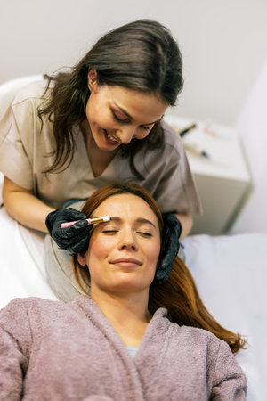 Beauty professional applying eyebrow tint to a woman's brows using a brush.の写真素材