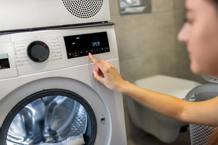 Close up view of cropped woman hand operating the handsettings button at modern automatic washing machine.の写真素材