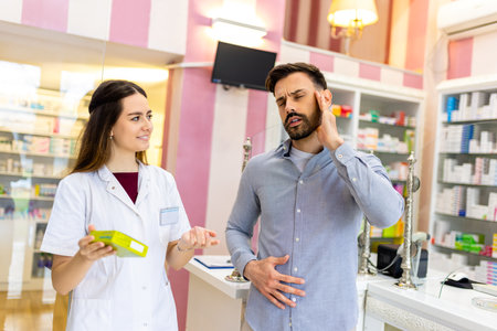 A pharmacy cashier is recommending medicine to a customer, while a professional pharmacist dispenses prescription medications in the pharmacy.の写真素材