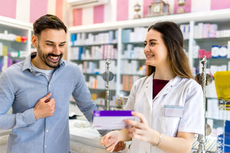 A pharmacy cashier is recommending medicine to a customer, while a professional pharmacist dispenses prescription medications in the pharmacy.の写真素材