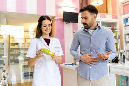 A pharmacy cashier is recommending medicine to a customer, while a professional pharmacist dispenses prescription medications in the pharmacy.の写真素材
