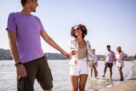 Young couple walking along the beach, enjoying each other's company and the sound of the waves. Holding hands and smiling, they share a peaceful and romantic moment by the shore.の写真素材