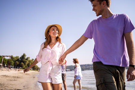 Young couple walking along the beach, enjoying each other's company and the sound of the waves. Holding hands and smiling, they share a peaceful and romantic moment by the shore.の写真素材