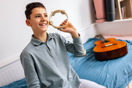 A young boy plays the tambourine with energy and enthusiasm while sitting on his bed, bringing rhythm and life to his cozy room.の写真素材