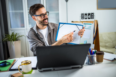 A young man participating in a video call from home, presenting a growth chart on his laptop screen. He is engaged and professional, using visual data to explain progress or business performance.の写真素材