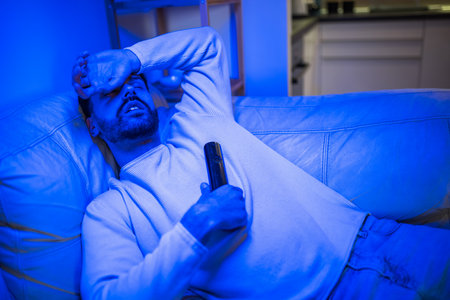 A young man has fallen asleep in front of the TV with the remote control still in his hand.の写真素材