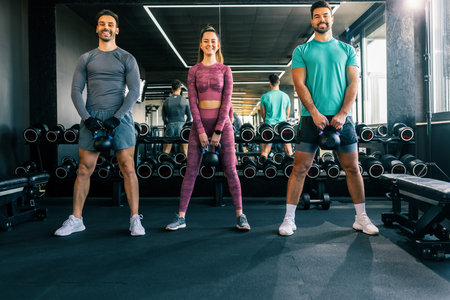 Two men and one woman lifting weights together in a modern gym.の写真素材