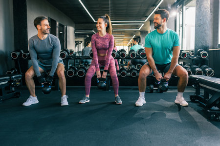 Two men and one woman lifting weights together in a modern gym.の写真素材