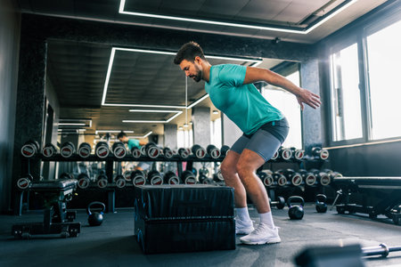 A fit young man captured mid-jump during an intense workout in a modern gym.の写真素材