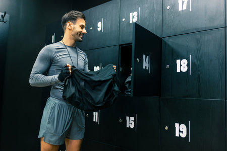 Fit man puts his stuff in the locker of the dressing room in the gym.の写真素材