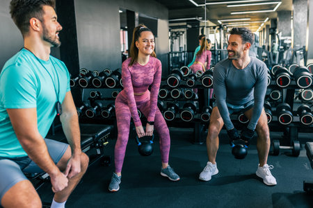 Two men and one woman lifting weights together in a modern gym.の写真素材