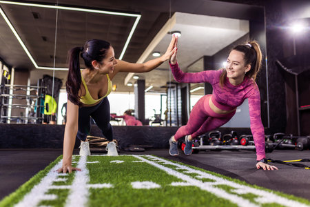 Two girl friends doing push ups in the gym. They high five.