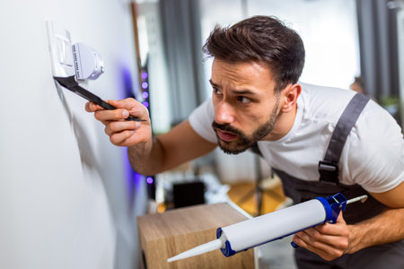 A young handyman is performing minor repairs in an apartment, applying silicone sealant with precision.の写真素材