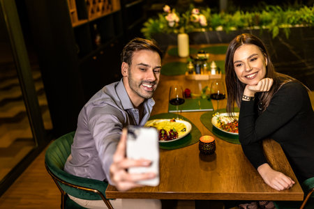 Young, happy beautiful couple taking selfie on a romantic dinner date at the restaurant.の写真素材