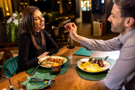 Young, beautiful couple feeds each other with food in a restaurant on a romantic dinner date.の写真素材