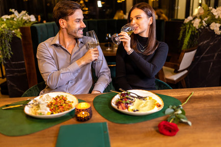 Young, happy couple in love drinks white wine in luxury restaurant on a romantic date .の写真素材