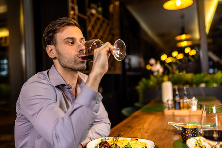 Elegant young man drinks red wine in a restaurant.の写真素材