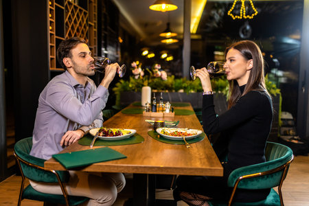 Young, happy couple in love drinks red wine in luxury restaurant on a romantic date.の写真素材