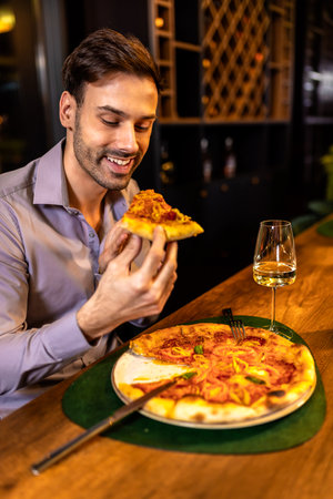 Young handsome man enjoys eating delicious pizza in restaurant.の写真素材