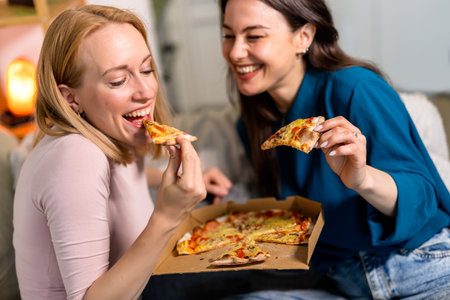Two best friends are having a cozy and fun night in the living room, enjoying slices of pizza and glasses of red wine. Laughter fills the space as they relax in comfy clothes, sharing stories and making memories.の写真素材