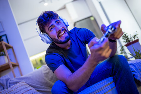 A young man sits comfortably at home, fully immersed in his gaming experience, holding a controller and focused on the screen in front of him. With his favorite game in play, heâs fully engaged in the digital world, living out virtual adventures and challenges.の写真素材