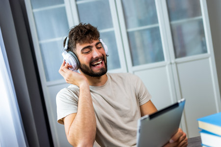 Young student is immersed in his studies, using a tablet while wearing headphones. Whether listening to a lecture, watching educational videos, or focusing on online research, he is fully engaged in the digital learning experience.の写真素材