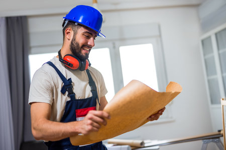 A young man works diligently on renovating his apartment, focusing on the installation of laminate flooring. With the right tools in hand, he carefully measures and fits the laminate panels into place, transforming the space with his DIY skills.の写真素材