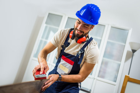 A young man works diligently on renovating his apartment, focusing on the installation of laminate flooring. With the right tools in hand, he carefully measures and fits the laminate panels into place, transforming the space with his DIY skills.の写真素材