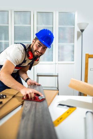 A young man works diligently on renovating his apartment, focusing on the installation of laminate flooring. With the right tools in hand, he carefully measures and fits the laminate panels into place, transforming the space with his DIY skills.の写真素材