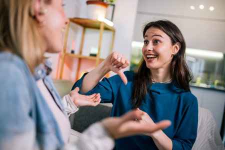 Two young girls are using sign language to talk to each other. One of them is wearing a hearing aid. They are smiling and enjoying the conversation.の写真素材