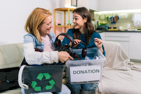 Two girls are holding a box with old computer parts, getting ready to recycle or donate them.の写真素材