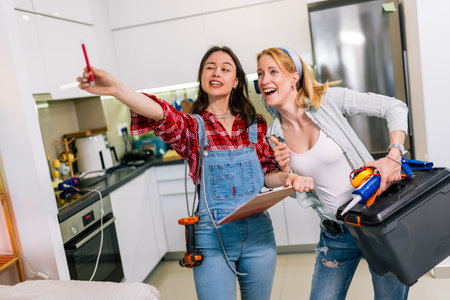 Two girls are standing in a room with tools in their hands, ready to start fixing and renovating the house.の写真素材
